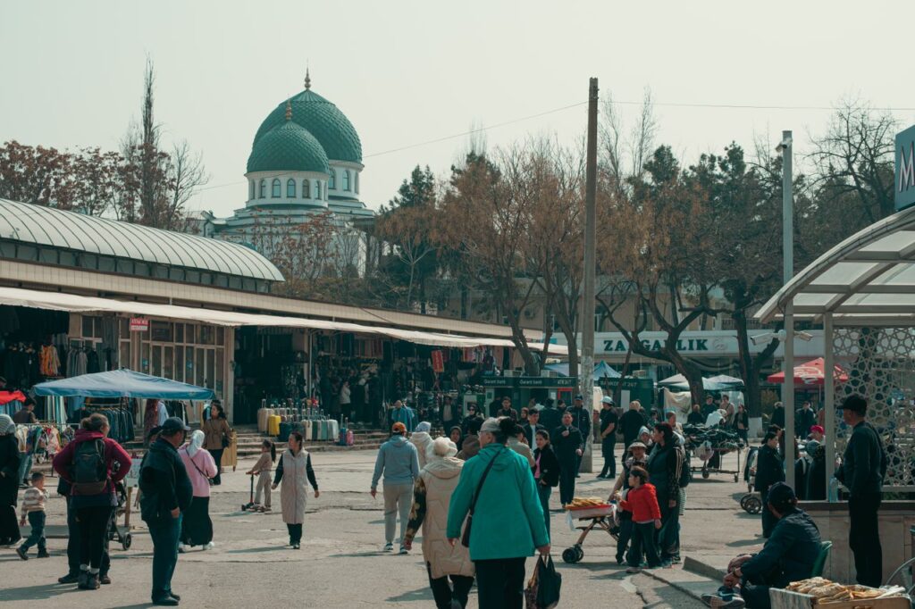 A bustling marketplace scene featuring diverse people and a mosque in the background in Uzbekistan.