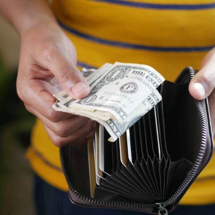 Close-up of a person's hands holding US dollar bills and a wallet.