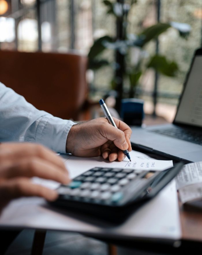 A person calculating finances with a calculator and pen on a desk indoors.