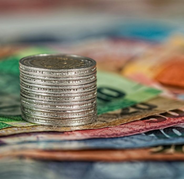A stack of coins on top of various colored banknotes, symbolizing finance and currency.