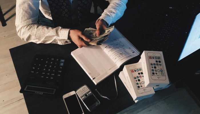 Businessman organizing finances with tech devices and cash on desk.