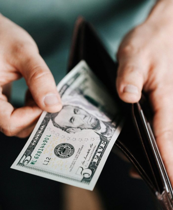 A person taking a five dollar bill from a wallet symbolizing personal finance and budget management.