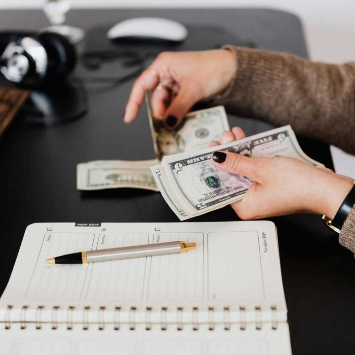 Woman counting cash at desk with notebook, pen, and headphones nearby.