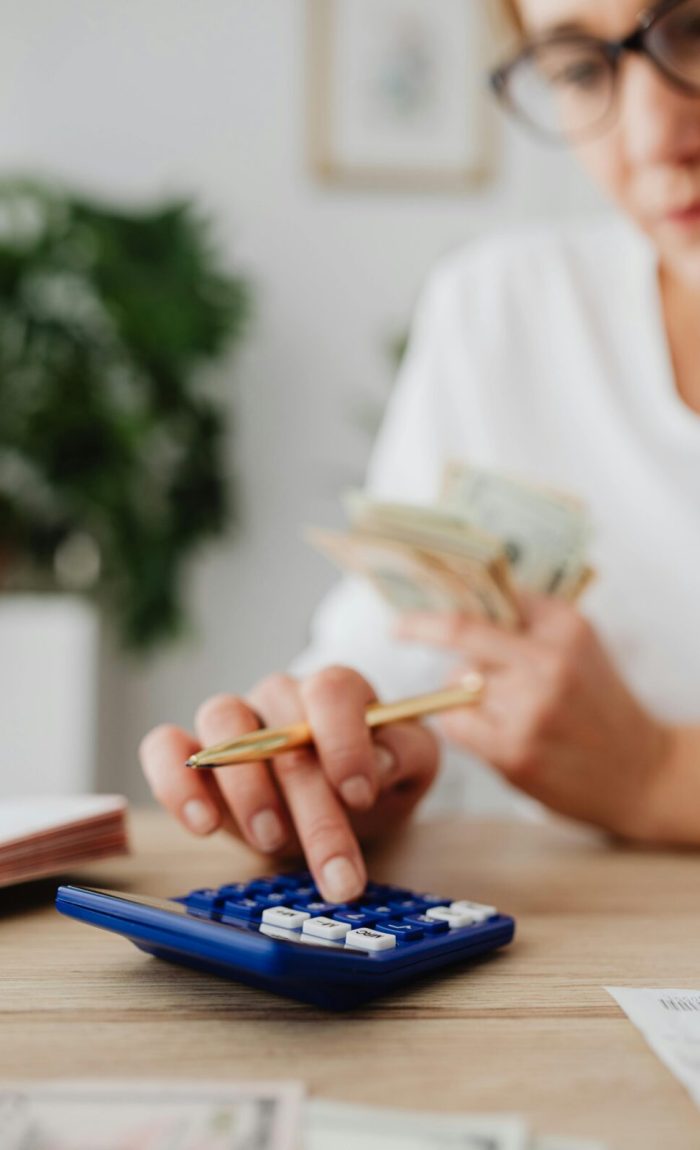 A woman uses a calculator and holds money, illustrating personal finance management.
