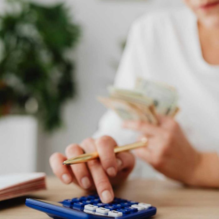 A woman uses a calculator and holds money, illustrating personal finance management.